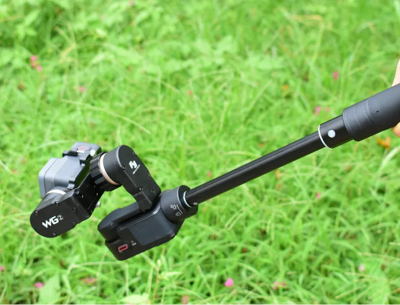 Black retractable aluminium selfie stick extended in hand next to a smartphone.