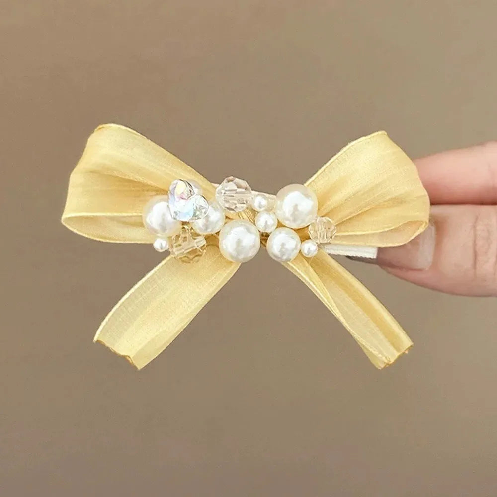 Yellow bow hair barrette with rhinestone and pearl accents on duckbill metal clip