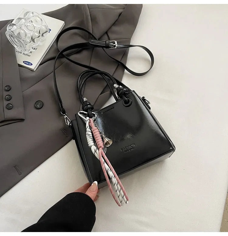 Women's PU one-shoulder bucket messenger bag in black with pendant, showing front view with single strap