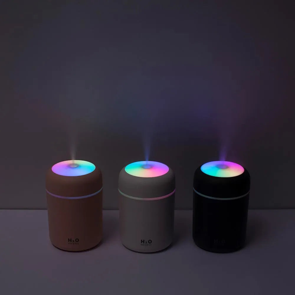 Pink USB desktop humidifier with colourful lights and water tank on wooden surface