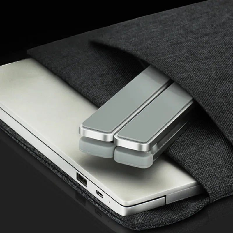 Folding aluminium laptop stand in silver, open and holding a laptop, with non-slip silicone pads visible