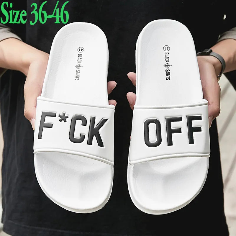Men's black open-toe slippers with a textured rubber sole and soft viscose upper, shown on a wooden floor.