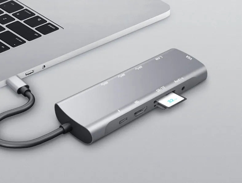 Grey aluminium USB-C docking station with HDMI, VGA, USB 3.0, and PD charging ports on a desk.