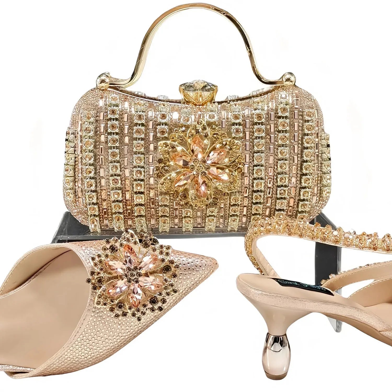 Women's black high heel shoes with rhinestone flowers and an ankle chain, next to a matching hard clutch bag.