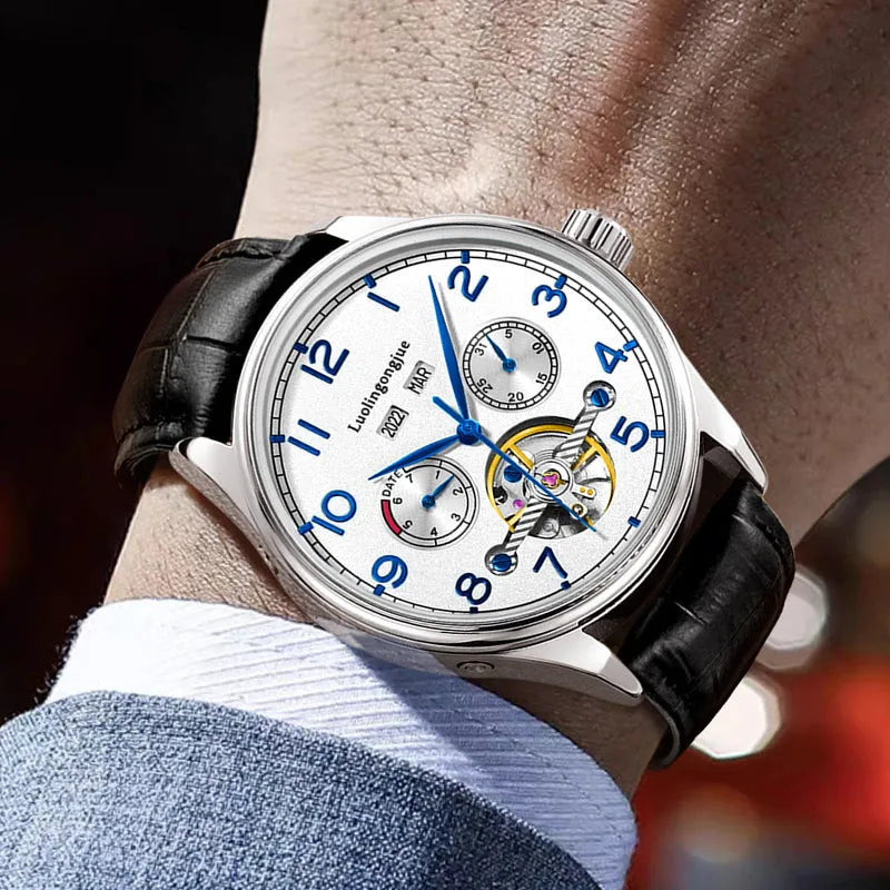 Men's stainless steel mechanical watch with leather strap and butterfly buckle on a business suit cuff.