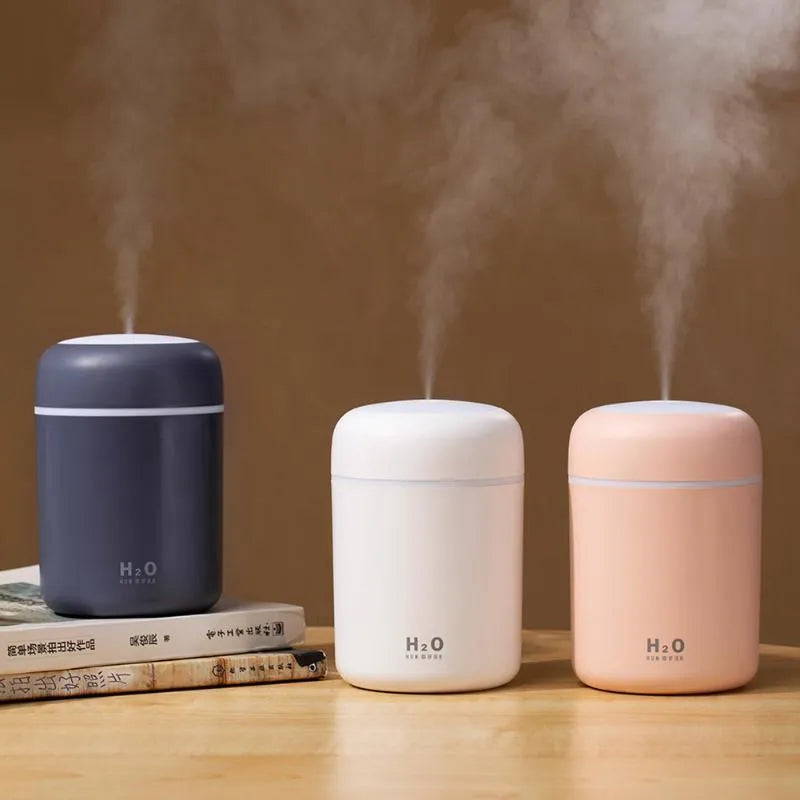 Pink USB desktop humidifier with colourful lights and water tank on wooden surface