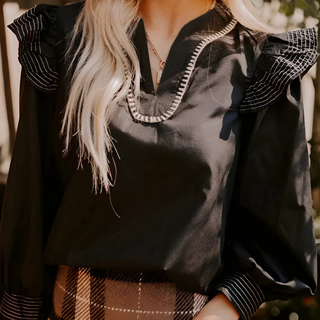 Black women's V-neck long sleeve blouse with white contrast stitching and a ruffle cuff detail