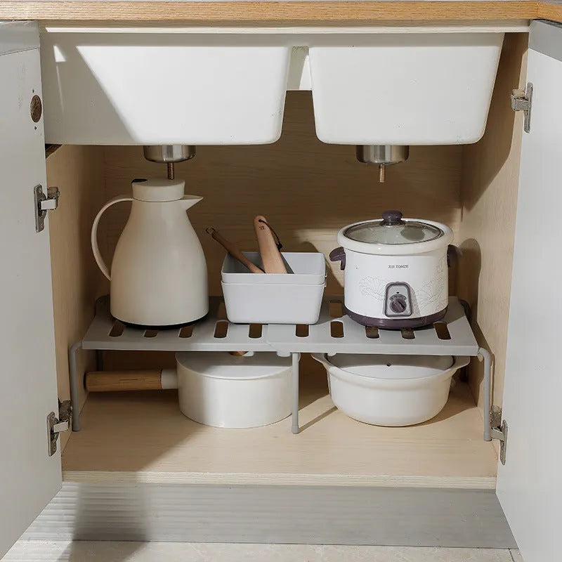 White telescopic plastic storage rack extended to full height with kitchen utensils organised on shelf
