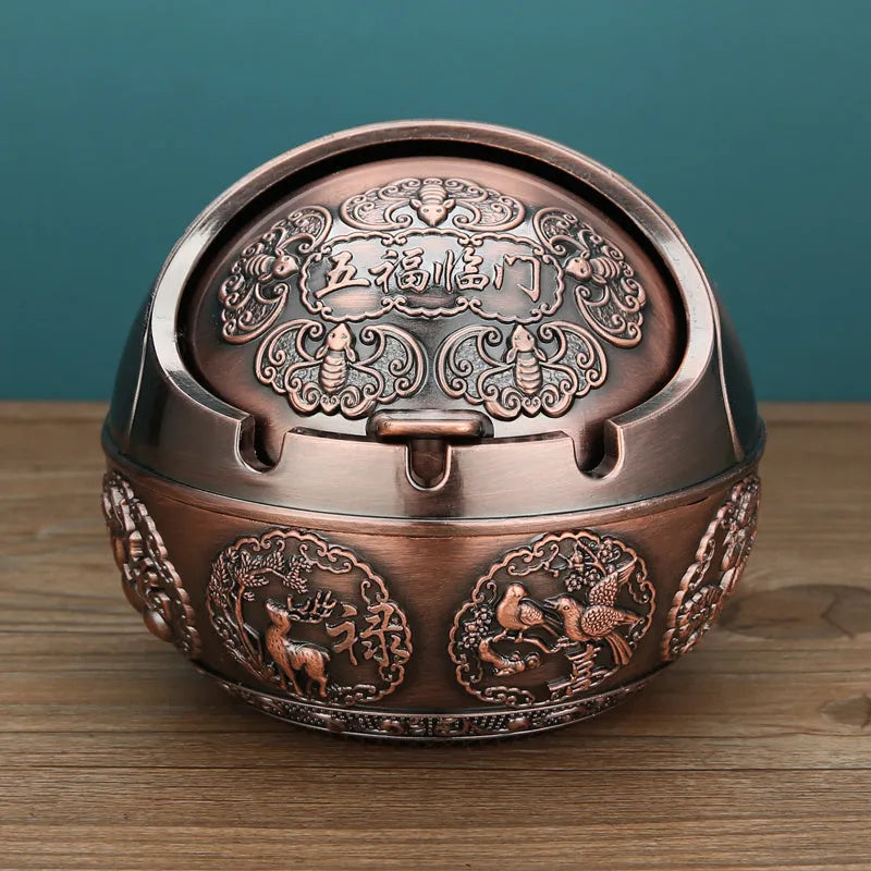 Bronze and red copper alloy decorative ashtray with smoke-extinguishing slot on a table.