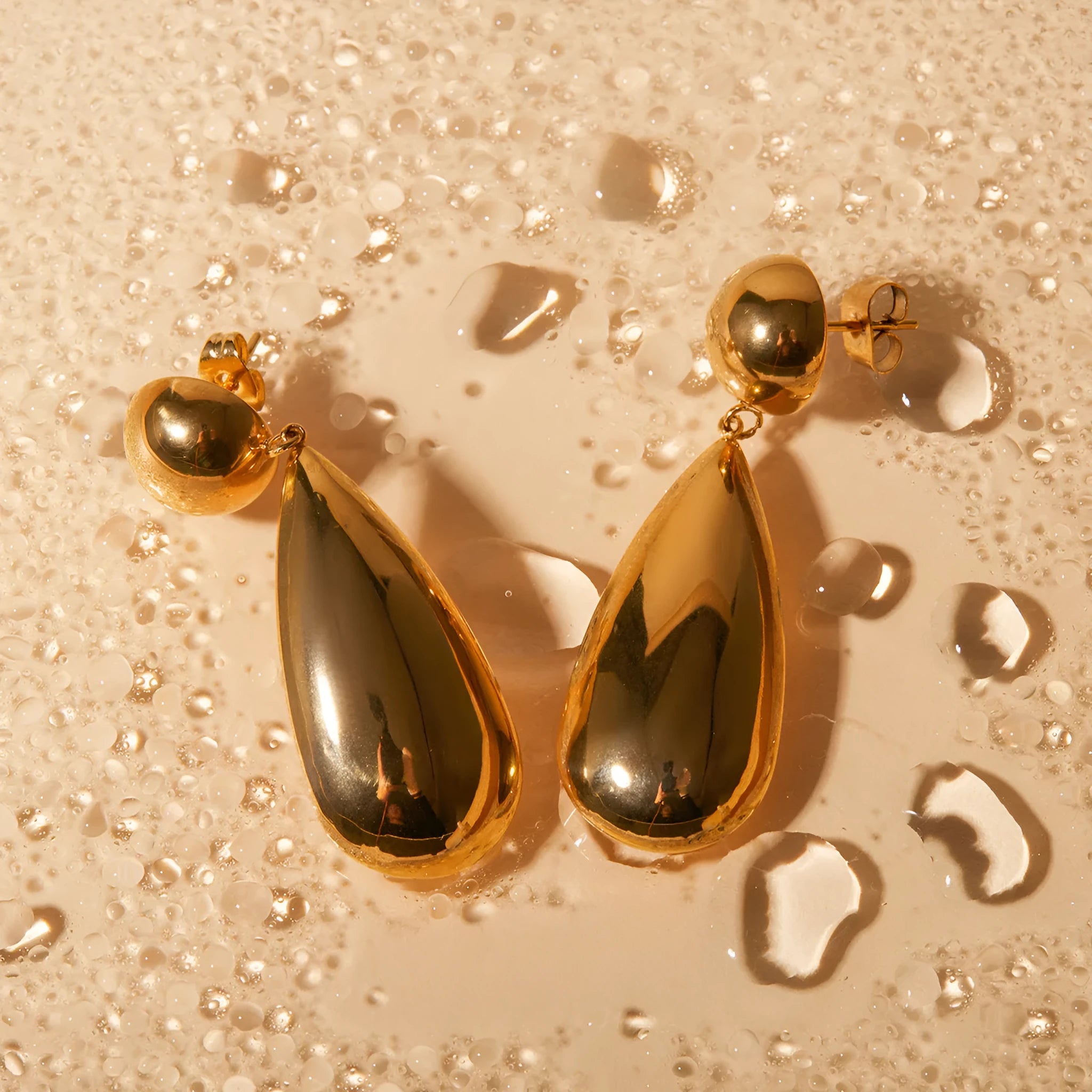 Gold stainless steel earrings with a geometric hemisphere and dangling water droplet pendant.
