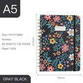 A5 spiral notebook with colourful floral cover design, lying open on a table.