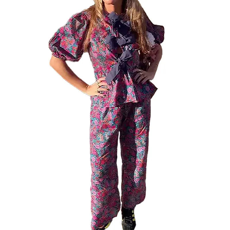 Women's floral print polyester trousers suit with tie-neck blouse and puff sleeves.