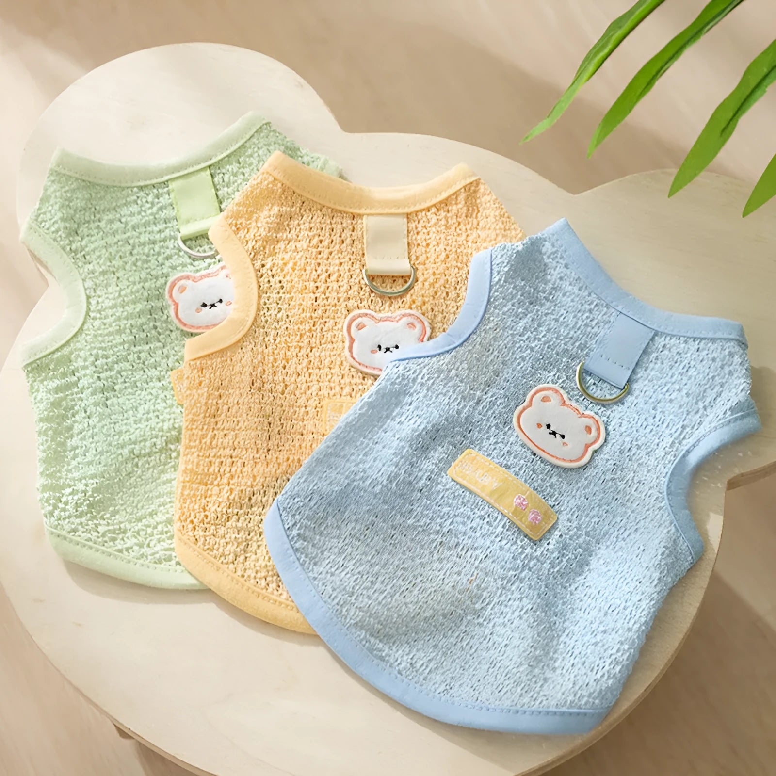 Green knitted cat clothing with a cartoon bear patch, showing hollowed-out breathable fabric.
