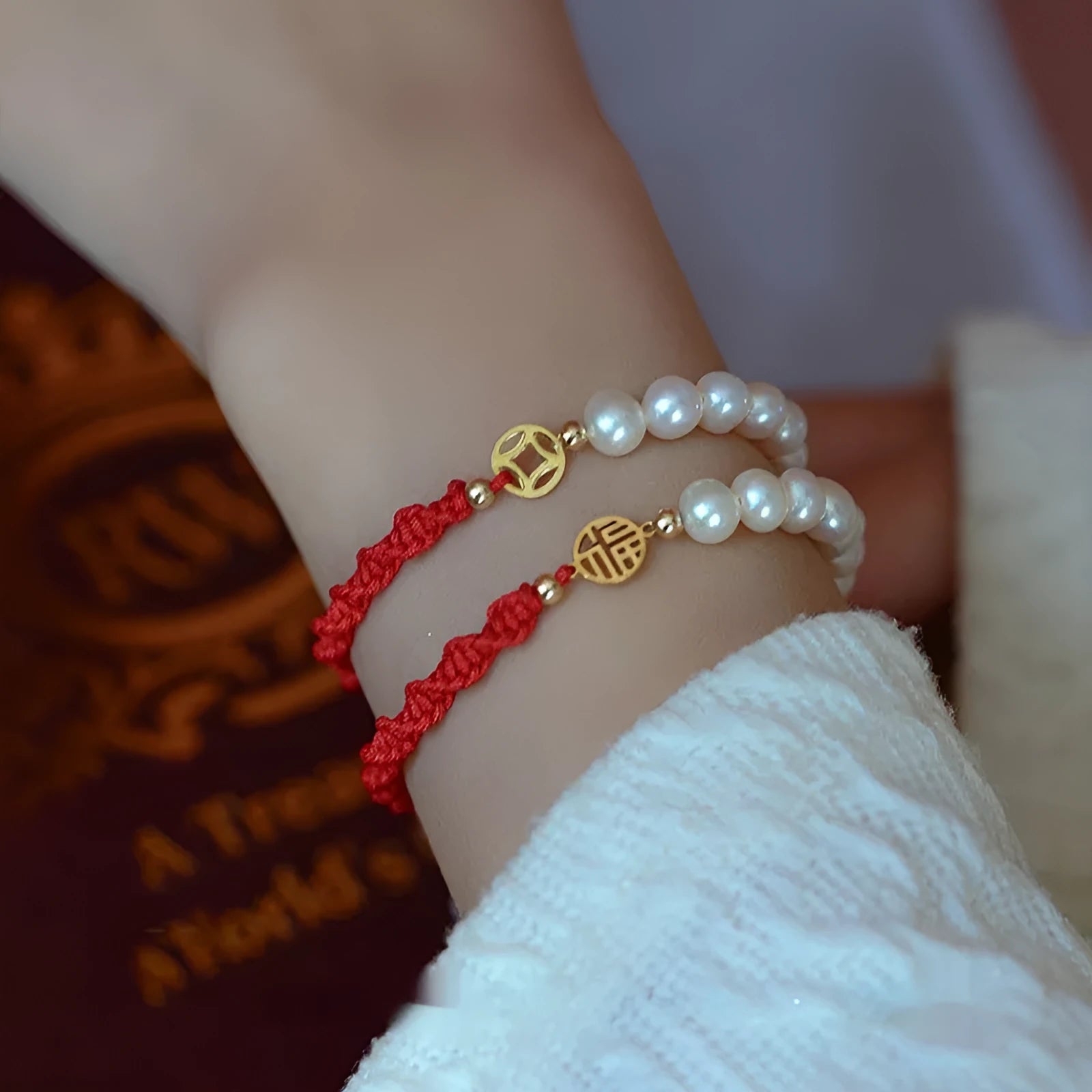 Close-up of a women's pearl and braided red rope bracelet with a gold-plated geometric fu character charm.