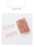 100 rose gold coloured heart-shaped metal paper clips in a box.