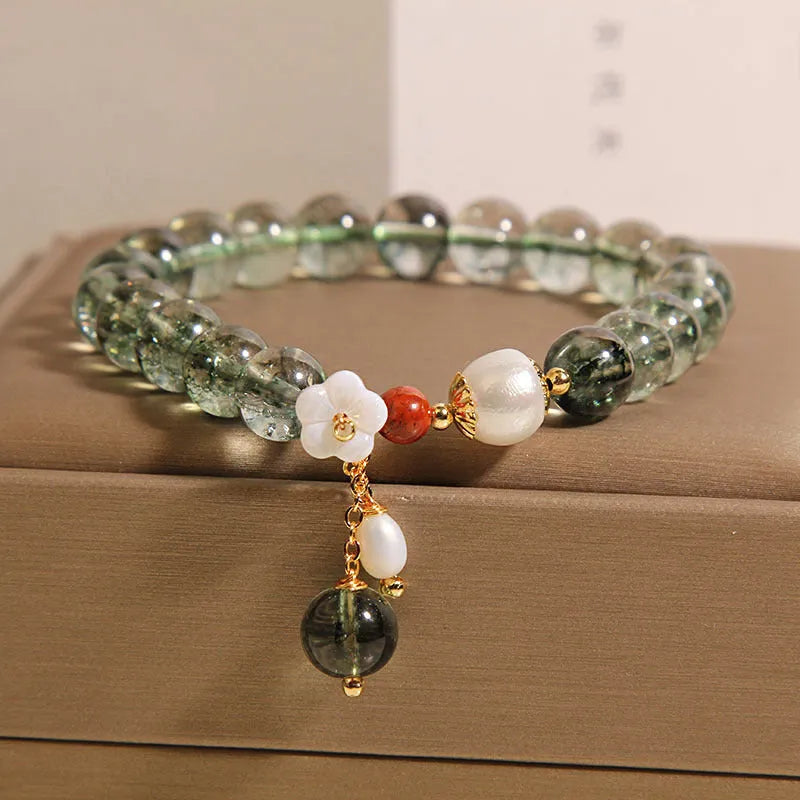 Women's green phantom quartz crystal bracelet with small shell flower accent on wrist.