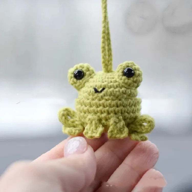 Handmade green plush frog car pendant hanging, showing woven cord and cartoon style.