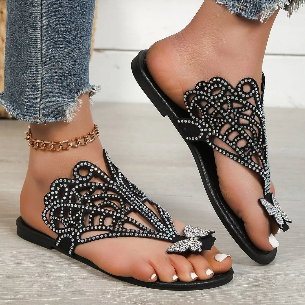 Women's black slip-on sandals with rhinestone decoration on the toe, showing flip-toe and flat rubber sole design.