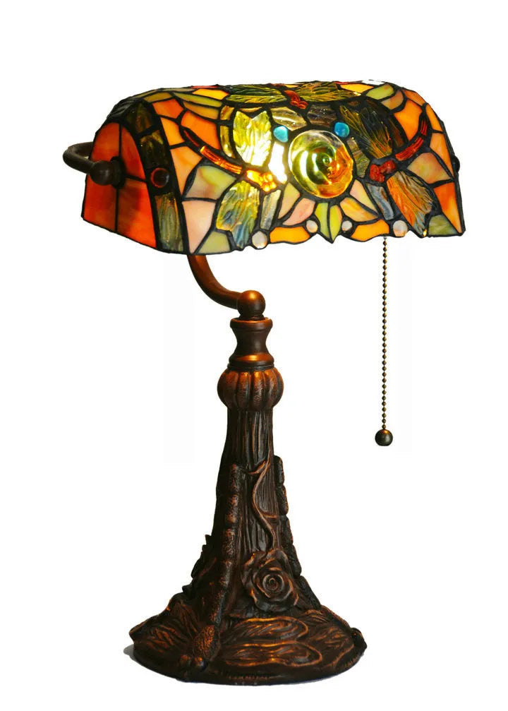 Tiffany style table lamp with colourful stained glass shade and resin base on a wooden desk