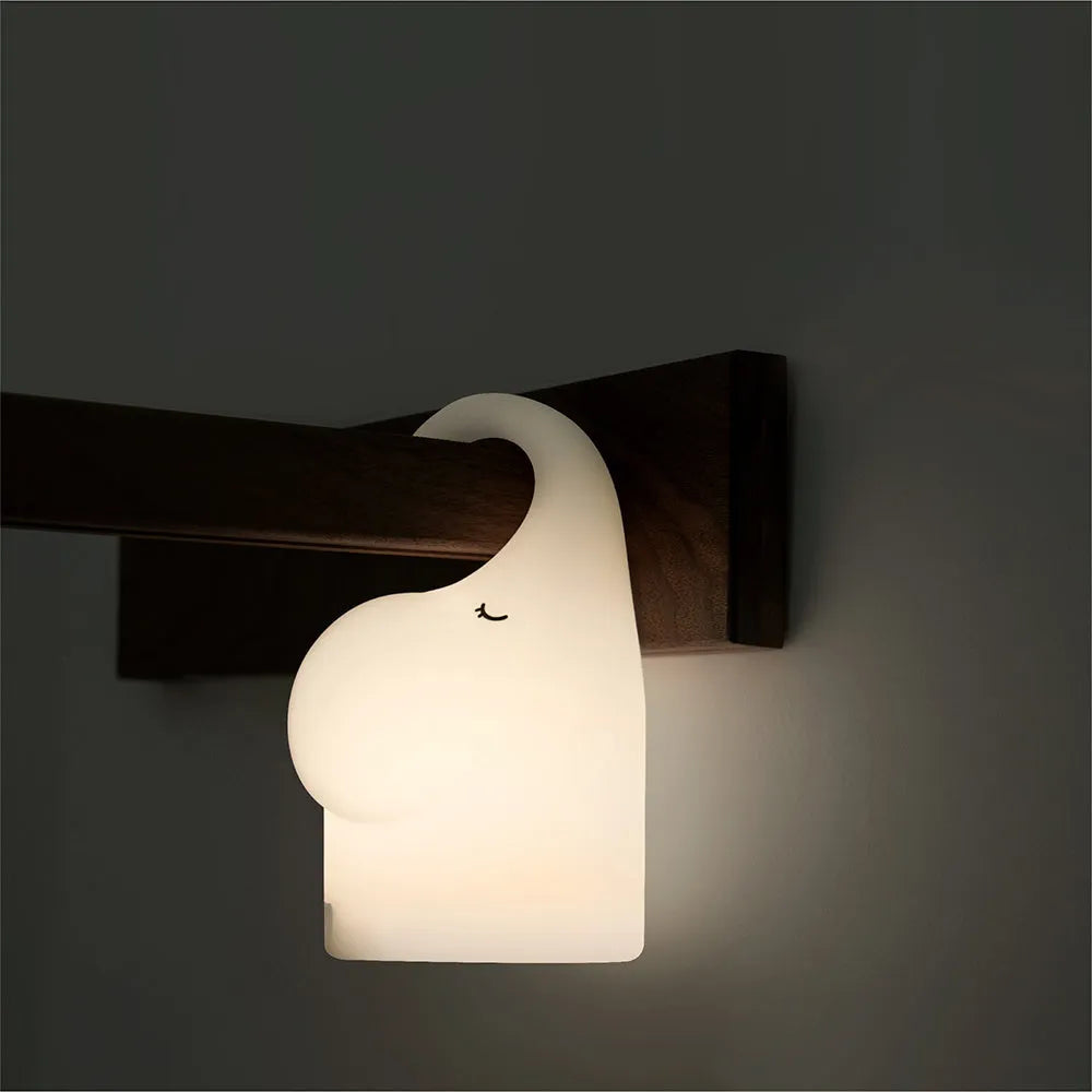 DOMI Elephant shaped silicone night light with warm white glow on a bedside table.