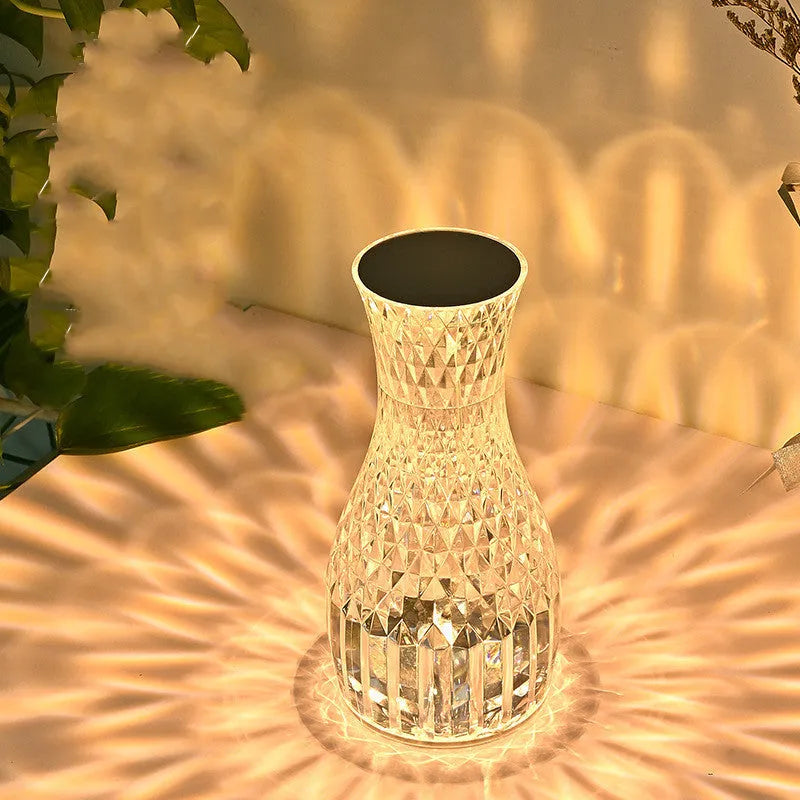 Vase-shaped transparent crystal bedside lamp with touch controls and LED lights on a table.
