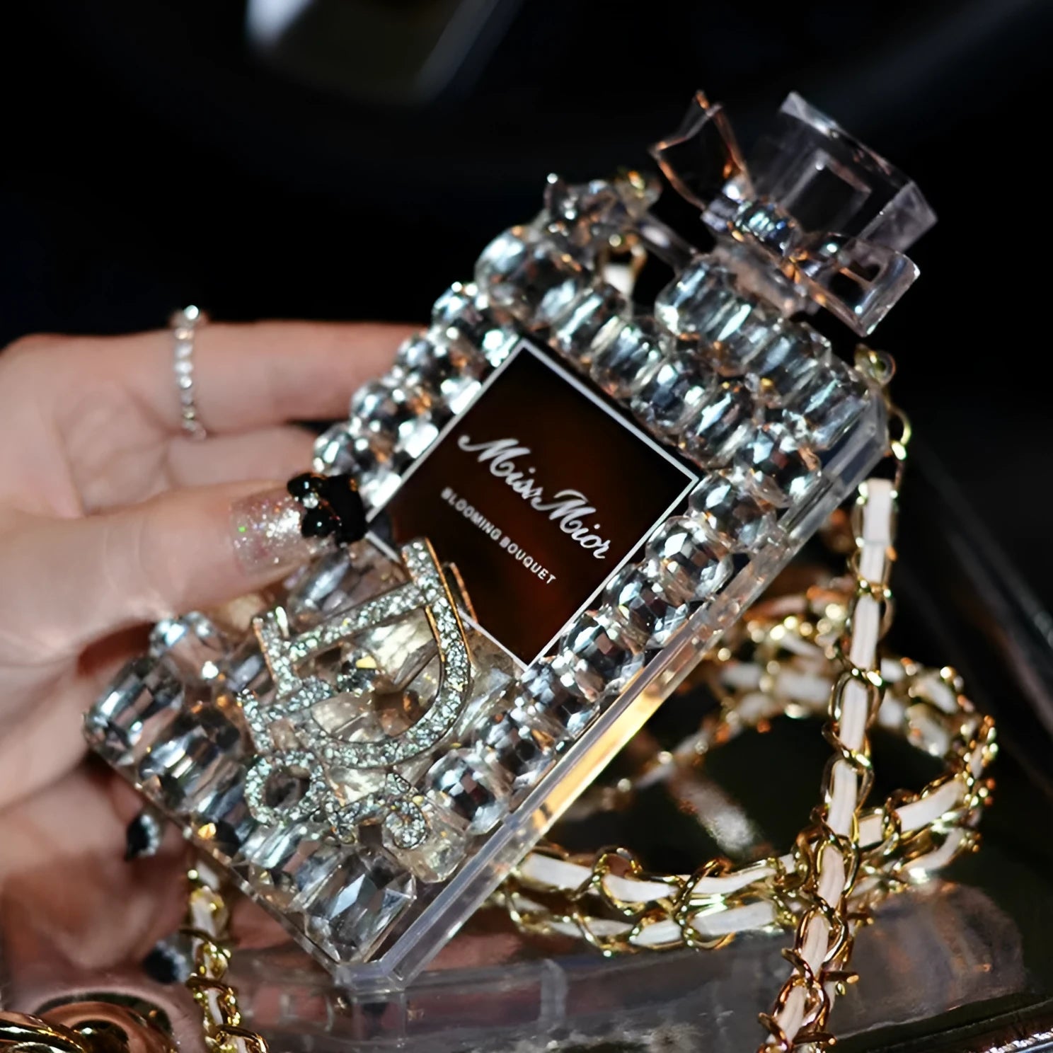 Perfume bottle design iPhone case with metal chain strap in black, shown on an iPhone.