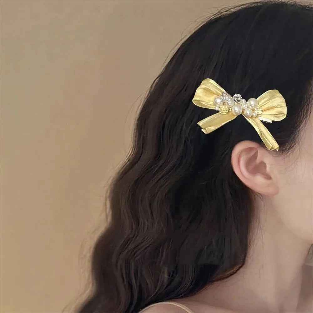 Yellow bow hair barrette with rhinestone and pearl accents on duckbill metal clip