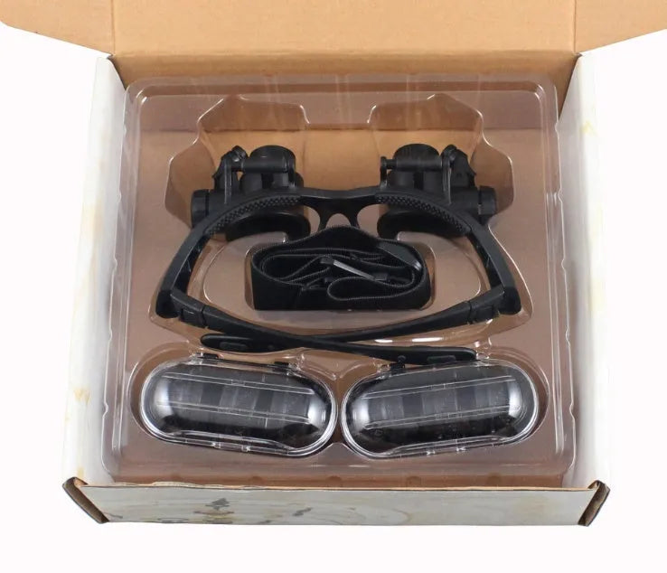 Black double eye magnifier glasses with LED lights and four sets of interchangeable lenses on a headband.