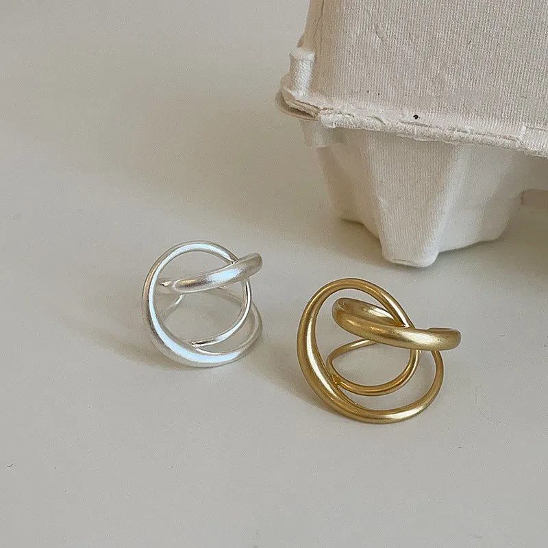 Geometric open ring with a 3D interlaced design in matte gold or silver metal.