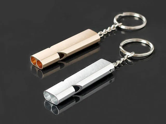 Close-up of a silver aluminium alloy double-hole outdoor survival whistle on a dark background.