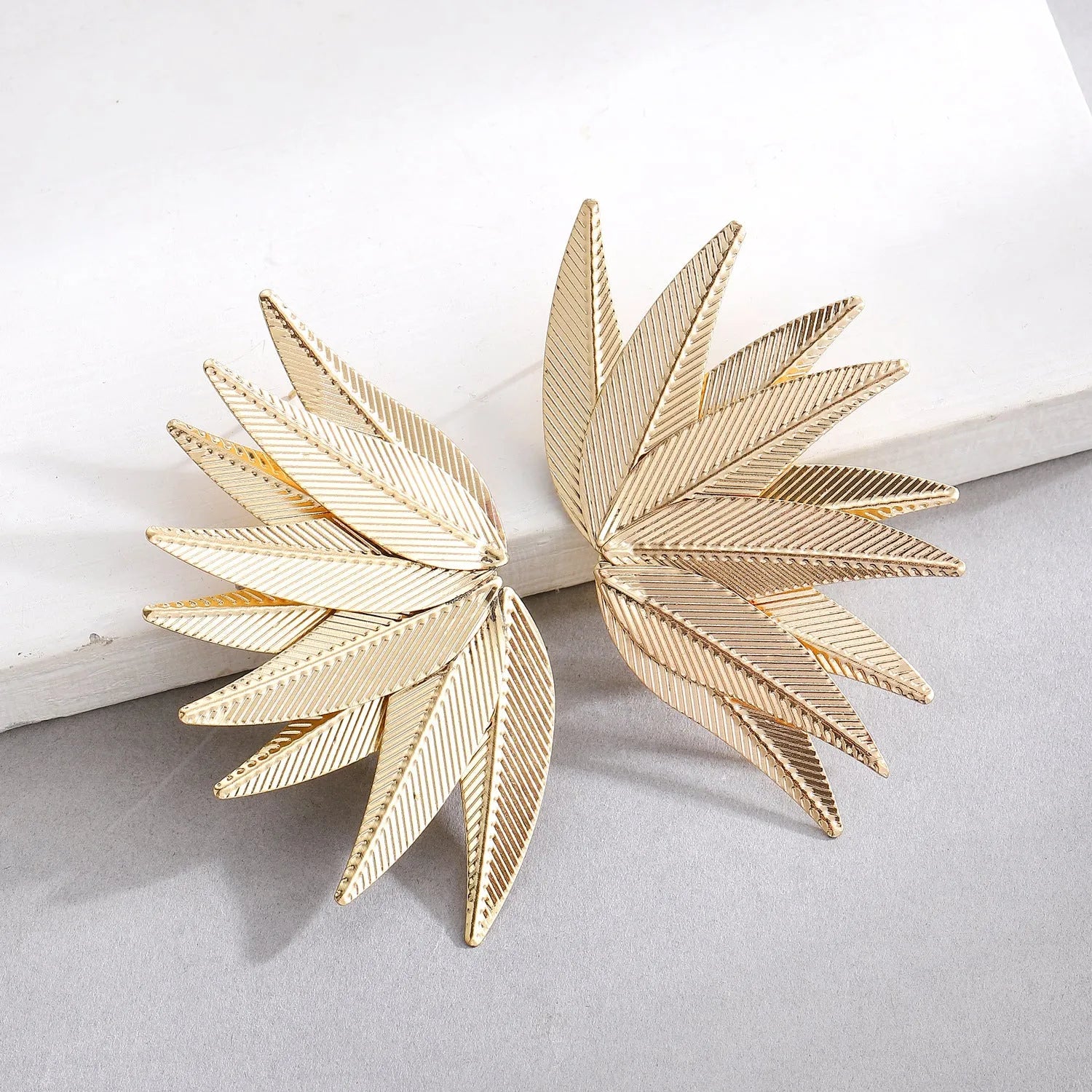 A pair of gold or white alloy earrings shaped like a leaf.