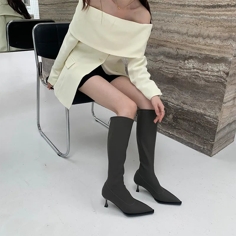 Women's black pointed toe below-the-knee boots with a stiletto heel and back zip on a neutral background.