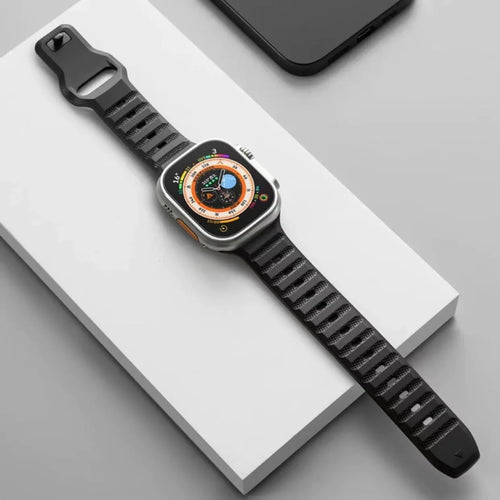 Black fluoro rubber Apple Watch band with T-buckle closure on a wrist, showing compatible Ultra model.