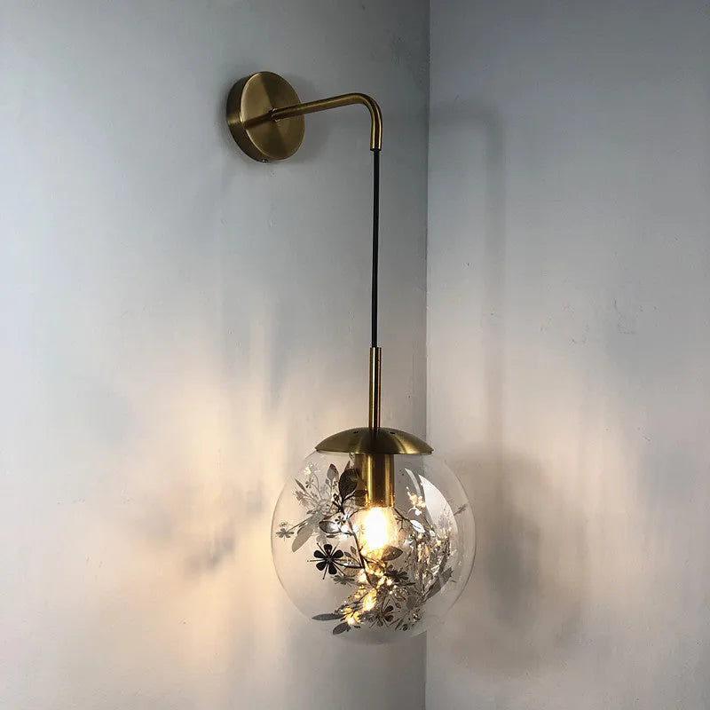 Modern small glass wall lamp in golden flower finish mounted on a bedroom wall.