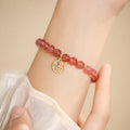 Glass strawberry quartz bead bracelet with a blessing card charm on a wrist.