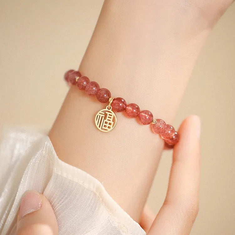 Glass strawberry quartz bead bracelet with a blessing card charm on a wrist.