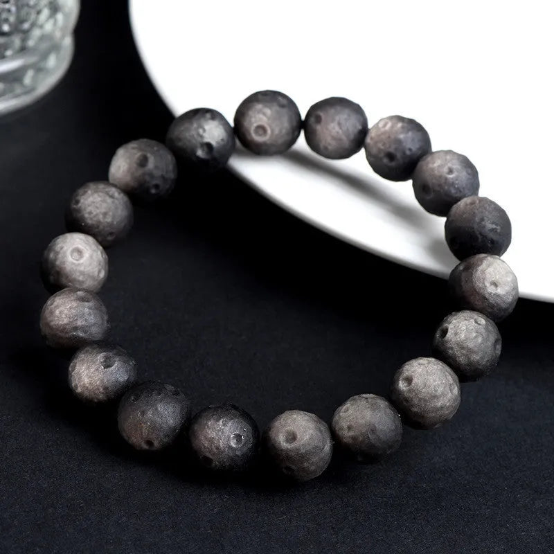Close-up of an obsidian crater ball bead bracelet in a gold meteorite finish, showing its textured spherical beads.
