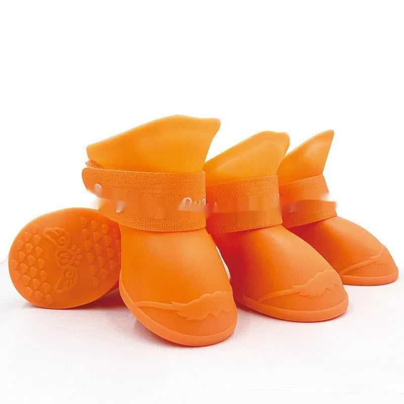 Set of four colourful rubber dog rain shoes with anti-slip soles on a wet surface.