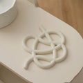 Irregular-shaped ceramic heat proof mat in grey with a curved hook for hanging, sitting on a wooden table.
