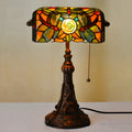 Tiffany style table lamp with colourful stained glass shade and resin base on a wooden desk