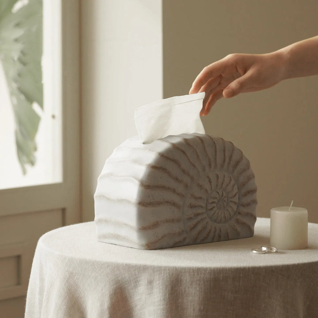 White conch ramble shell design resin tissue box holder on a table.