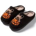 Black and white plush Halloween pumpkin slippers with textured rubber soles on a wooden floor.