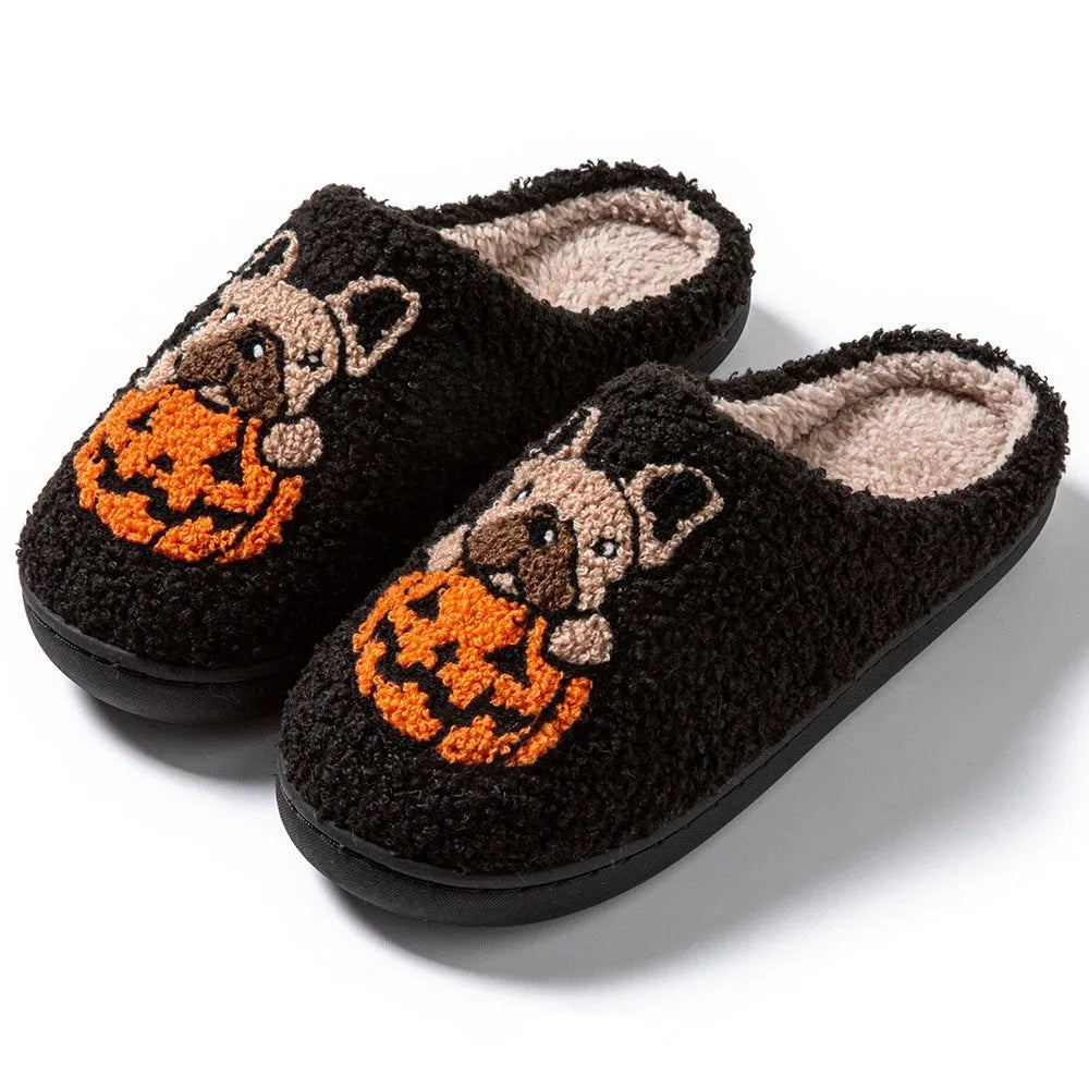 Black and white plush Halloween pumpkin slippers with textured rubber soles on a wooden floor.