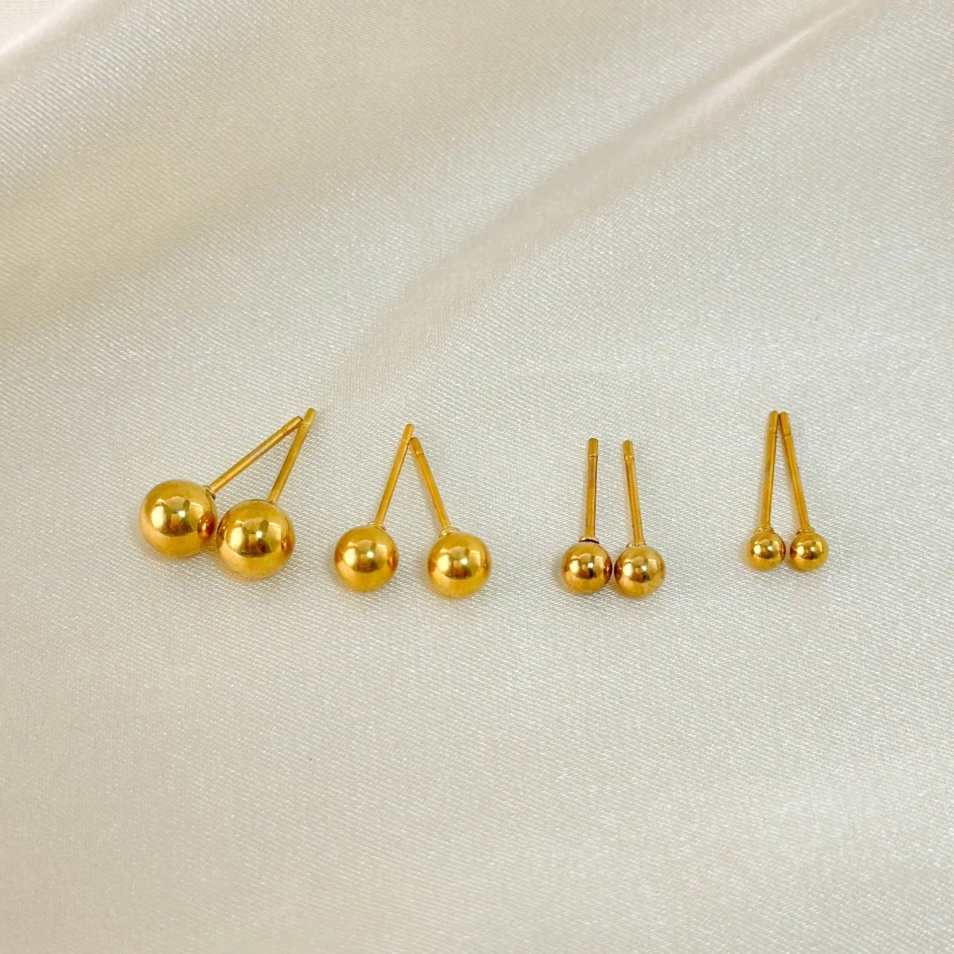 Close-up of a simple gold ball stud earring on a titanium steel post against a plain background.