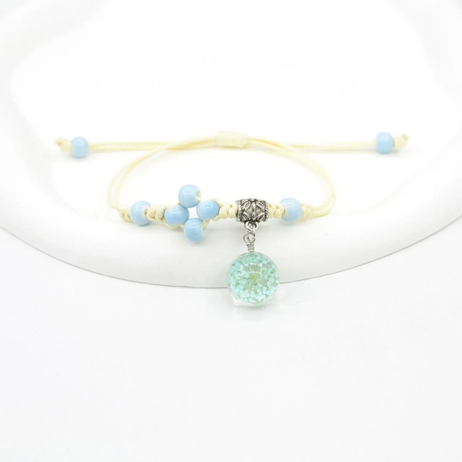 Close-up of a hand-woven glass bracelet with large 1.4cm beads containing real dried flowers and lace floral detailing.