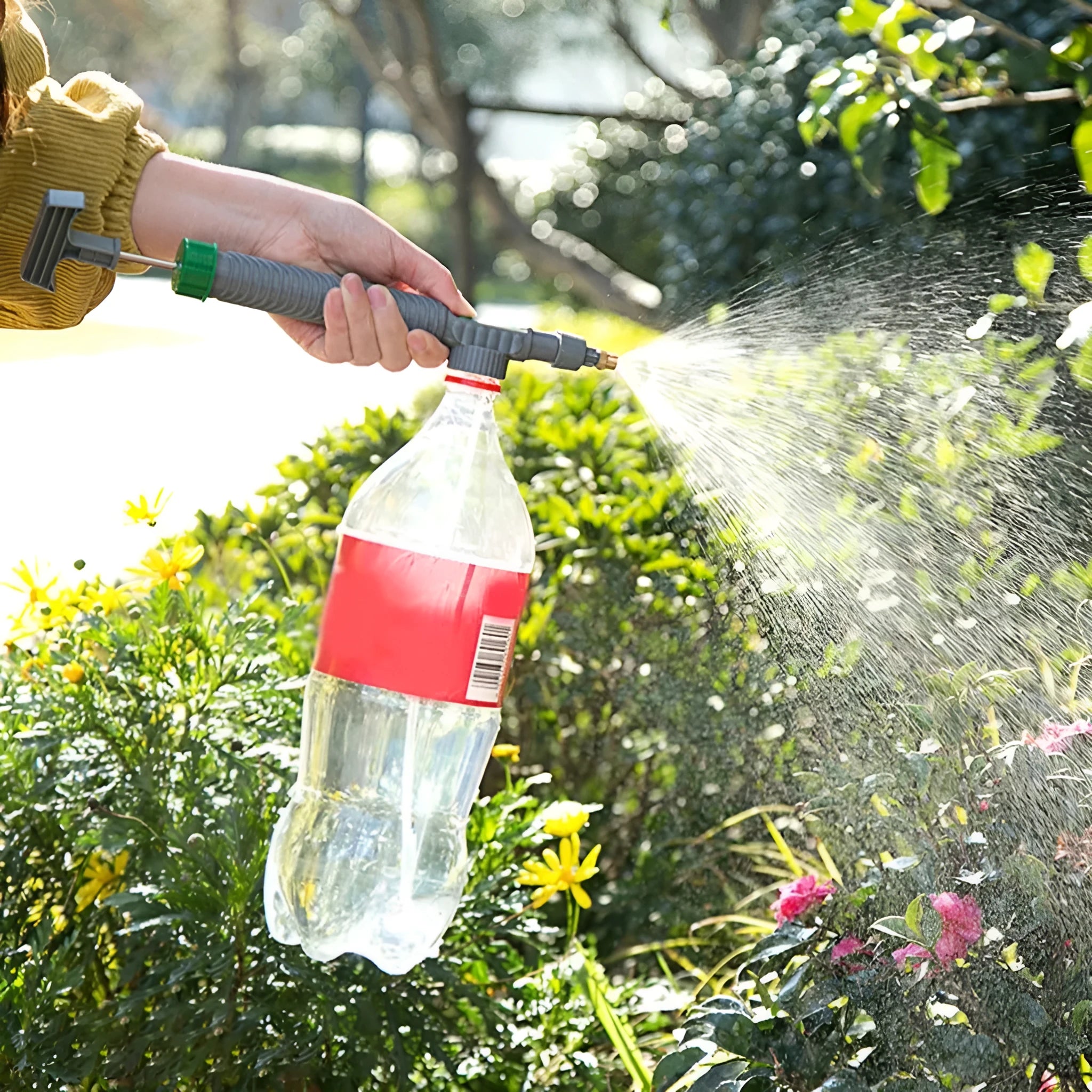 Plastic watering sprayer nozzle with extension tube attached to a large clear beverage bottle.
