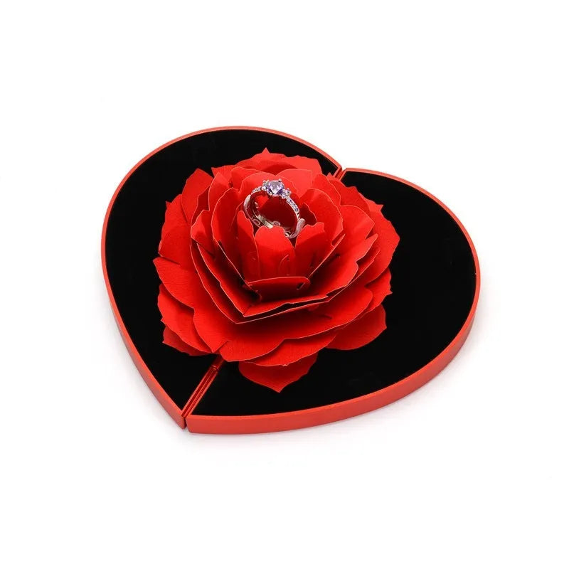 Red heart-shaped rotating ring box with 3D white rose decoration on top.