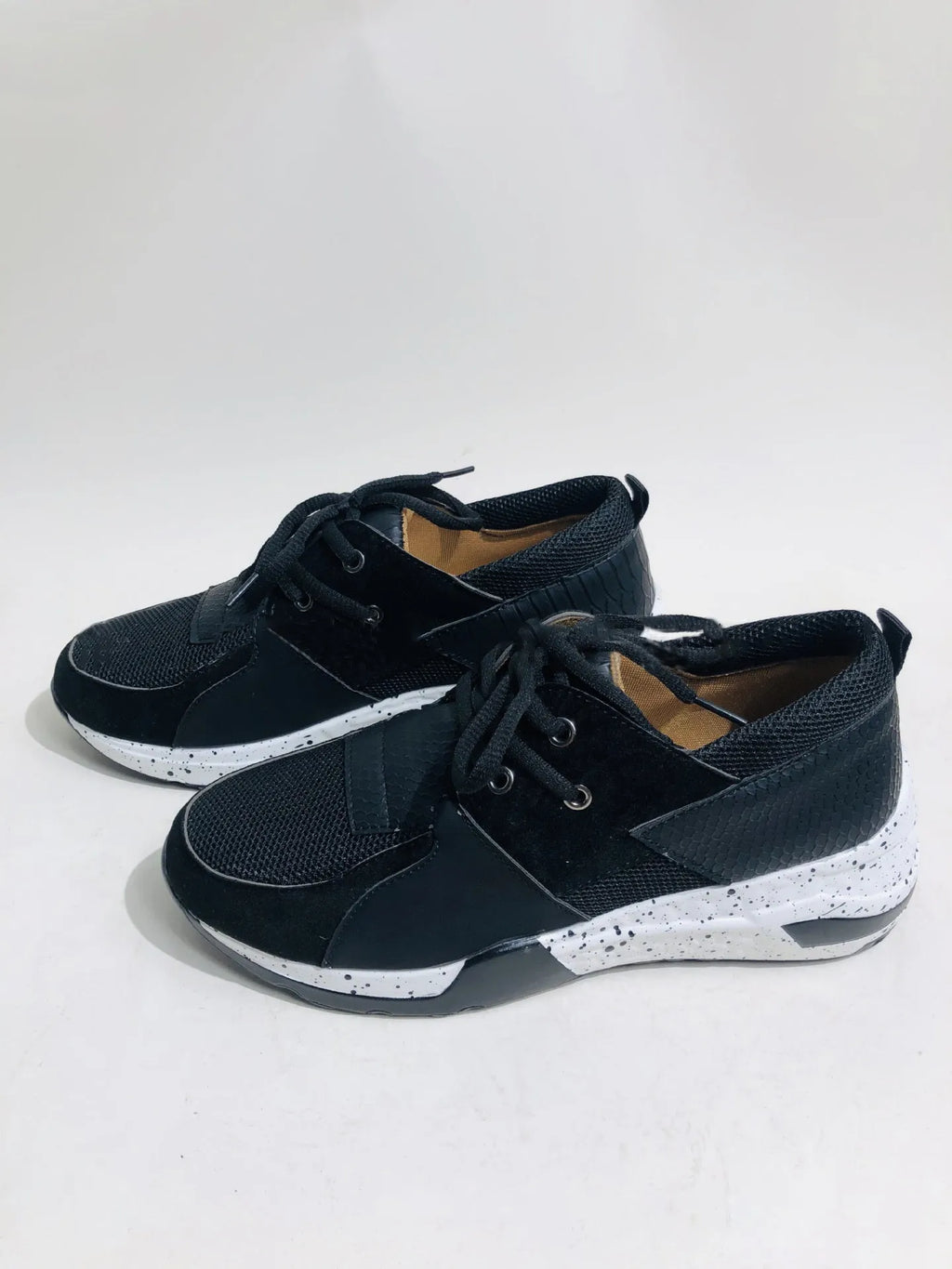 Women's black suede wedge sneakers with a round toe and low-cut design on a wooden floor.