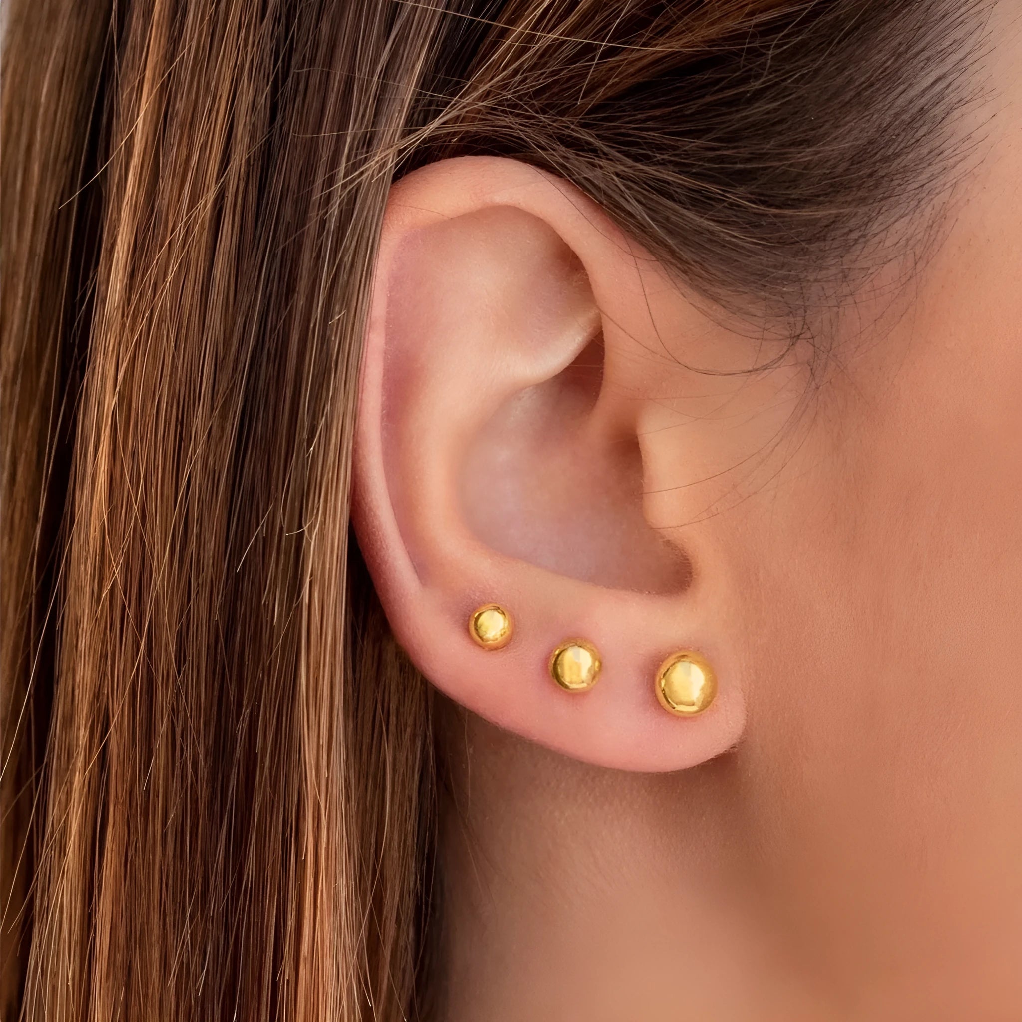 Close-up of a simple gold ball stud earring on a titanium steel post against a plain background.
