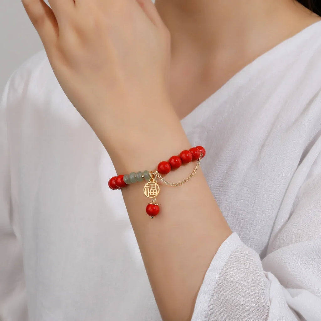 Women's handmade cinnabar bracelet with fu character charm, jade spacer beads, and red sand tassel detail